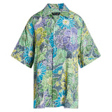 A short-sleeved, button-down Hawaiian-style shirt displayed on a white background. The fabric has an all-over, densely packed floral pattern that uses a crackled batik-style print on a muted blue-gray background. The flowers and leaves are colored in shades of light blue, turquoise, lime green, and lavender purple. The shirt has a camp collar and dark buttons.
