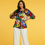 Woman wearing a colorful floral top and white pants on a yellow background
