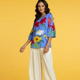 Woman wearing a colorful floral top and white pants on a yellow background