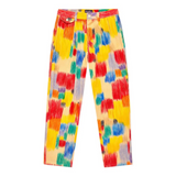 A pair of tailored, pleated trousers displayed flat on a white background. The pants are made of a light yellow corduroy fabric printed with bold, abstract pattern of vertical brushstrokes and rectangular shapes in bright red, yellow, blue, and green.