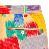 A close-up view of the back pocket area of the brightly colored trousers. The corduroy fabric features the abstract pattern in red, yellow, blue, and teal. A single, small white button secures the horizontal back welt pocket. A belt loop above the pocket features a thin stripe of red, blue, and green.