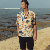 Man wearing a colorful patterned shirt and black shorts standing on a beach.