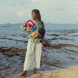 Person wearing a colorful shirt and white pants standing on a beach.