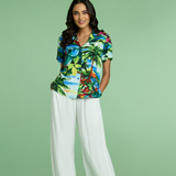 Woman wearing a tropical-themed button down shirt with color and pants of the same print on a green background