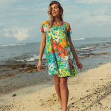 Woman in a colorful floral dress standing on a beach with ocean in the background