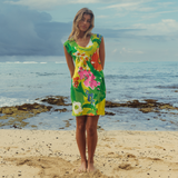 Woman in a colorful floral dress standing on a beach with ocean in the background