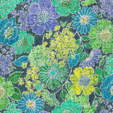 A close-up view of the fabric pattern. It is a dense, batik-style print of various large and small stylized flowers and leaves on a dark blue-gray background. The colors include lime green, turquoise, lavender purple, and bright yellow, with thin white lines outlining the elements. The entire pattern has a characteristic fine, crackled texture, typical of batik.