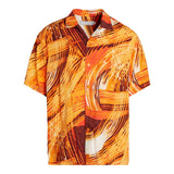 This image shows a short-sleeved collared shirt with an abstract, energetic pattern that looks like swirling brushstrokes. The colors are warm and tropical, primarily featuring bright orange, deep burnt orange, and warm yellow-gold, and the shirt is displayed flat against a white background.