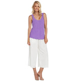 This is a full-length product photo of a woman with blonde hair, smiling directly at the camera. She is wearing a simple, loose-fitting bright purple tank top paired with white, wide-leg cropped culottes and nude high-heeled sandals.