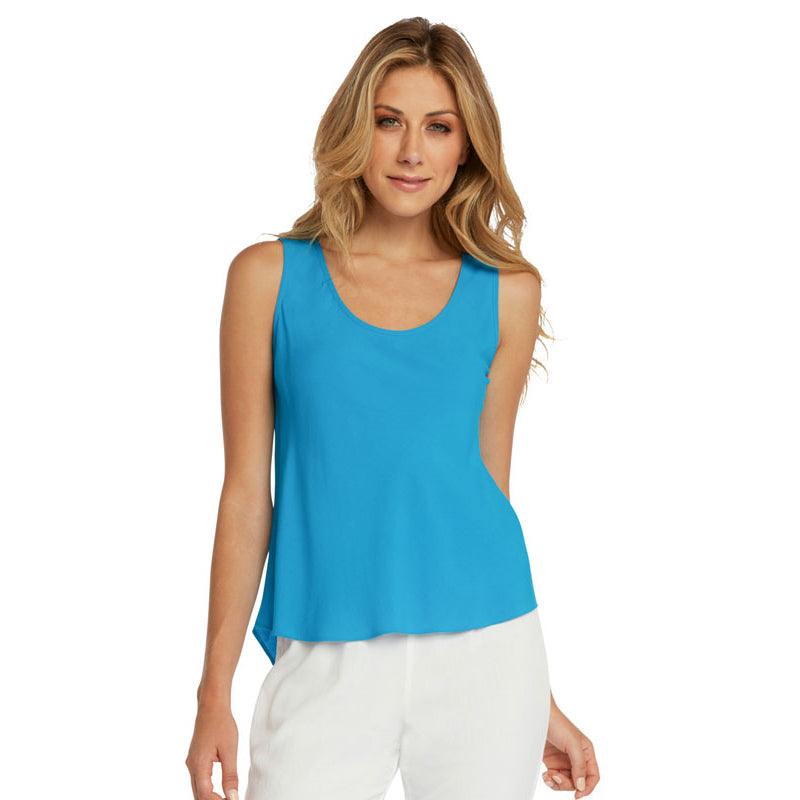 This is a product photo of a woman with long blonde hair, smiling directly at the camera while wearing a bright turquoise blue tank top. The top has a scoop neck and a loose, flowing fit that is slightly longer on the side. She is wearing white pants and is standing against a plain white background.