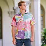 This is an outdoor lifestyle shot of the same young man wearing the brightly patterned shirt and dark pants, standing in front of a white arched structure. He is looking off to the side, with the open-collar shirt and its colorful floral pattern as the main focus.