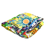 This image shows the quilt or blanket folded into a thick rectangle, highlighting the rich layers of the colorful patchwork design with a prominent yellow panel featuring a large blue and orange floral pattern.