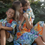 Mother and two young sons wear colorful floral print attire. Laughing and playing in yard.