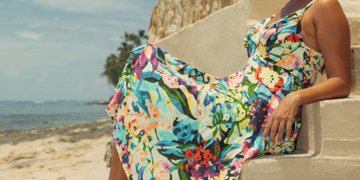 Colorful floral dress on model sitting on steps on beach.