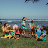 Family of four gathered on the lawn which is beach front. Spending time together in their aloha attire which are colorful floral prints.