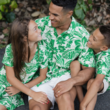 Family of four wearing matching green and white floral outfits sitting outdoors.