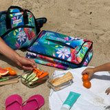 Colorful floral cooler bags on sand with snacks and a towel.