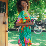 Woman in a colorful dress standing outdoors with greenery and a bicycle in the background