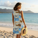 Woman in a patterned dress holding a hat on a beach with mountains in the background