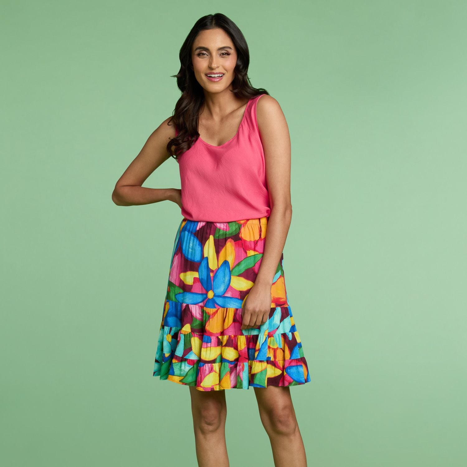Woman wearing a pink top and colorful floral skirt on a green background