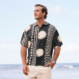 Man wearing a black and white patterned shirt standing on a beach.