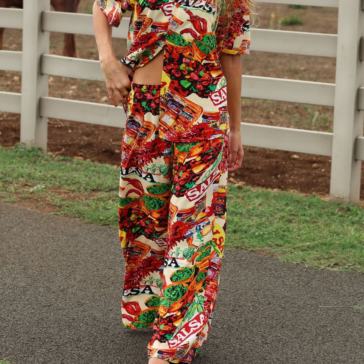 Person wearing a colorful candy-themed outfit walking on a path with a white fence in the background.