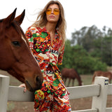 Woman in a colorful outfit standing next to a horse, wearing sunglasses.