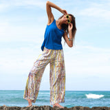 Woman in blue top and colorful pants standing on a rock by the ocean