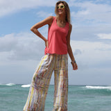 Woman in pink top and colorful pants standing on a beach with ocean and sky in the background