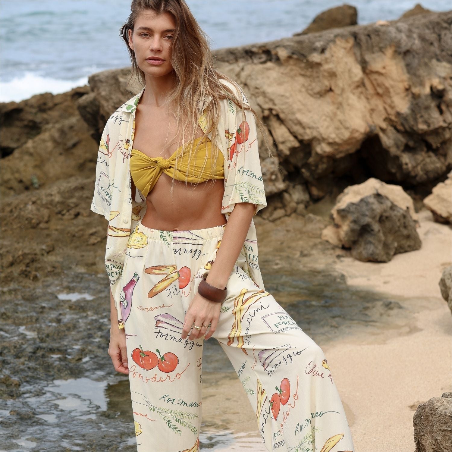 Mujer con un atuendo estampado de pie en una playa rocosa.
