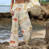 Una persona que lleva pantalones anchos con estampado de motivos alimenticios está de pie en una playa rocosa.