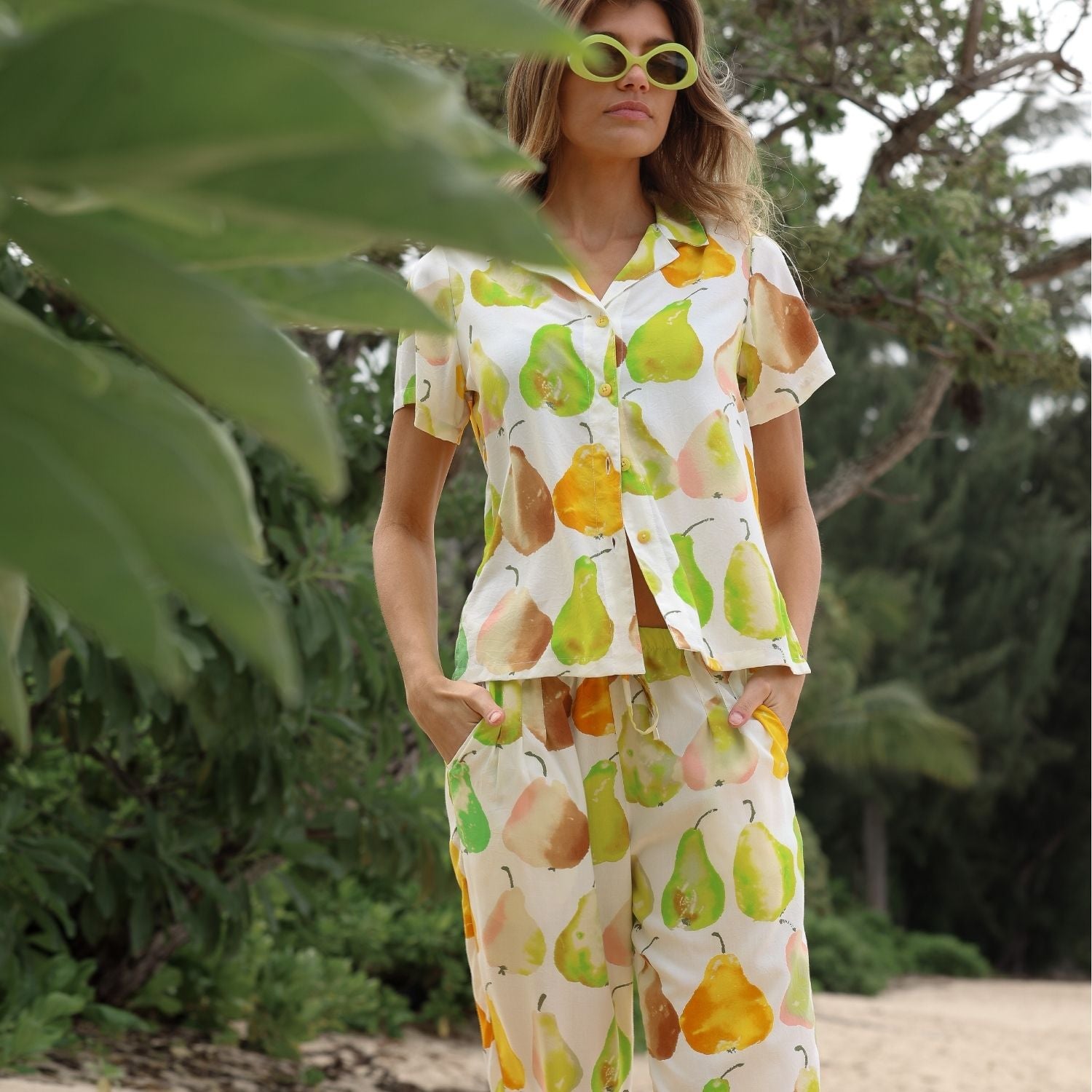 Femme vêtue d'une tenue colorée à motifs de poires, debout à l'extérieur, avec de la verdure en arrière-plan.