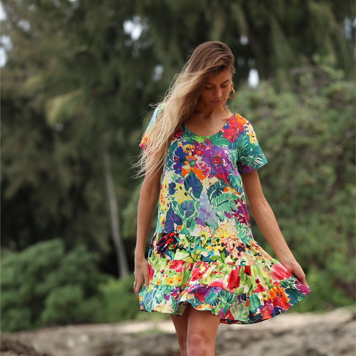 Femme vêtue d'une robe fleurie colorée, debout à l'extérieur, avec des arbres en arrière-plan.