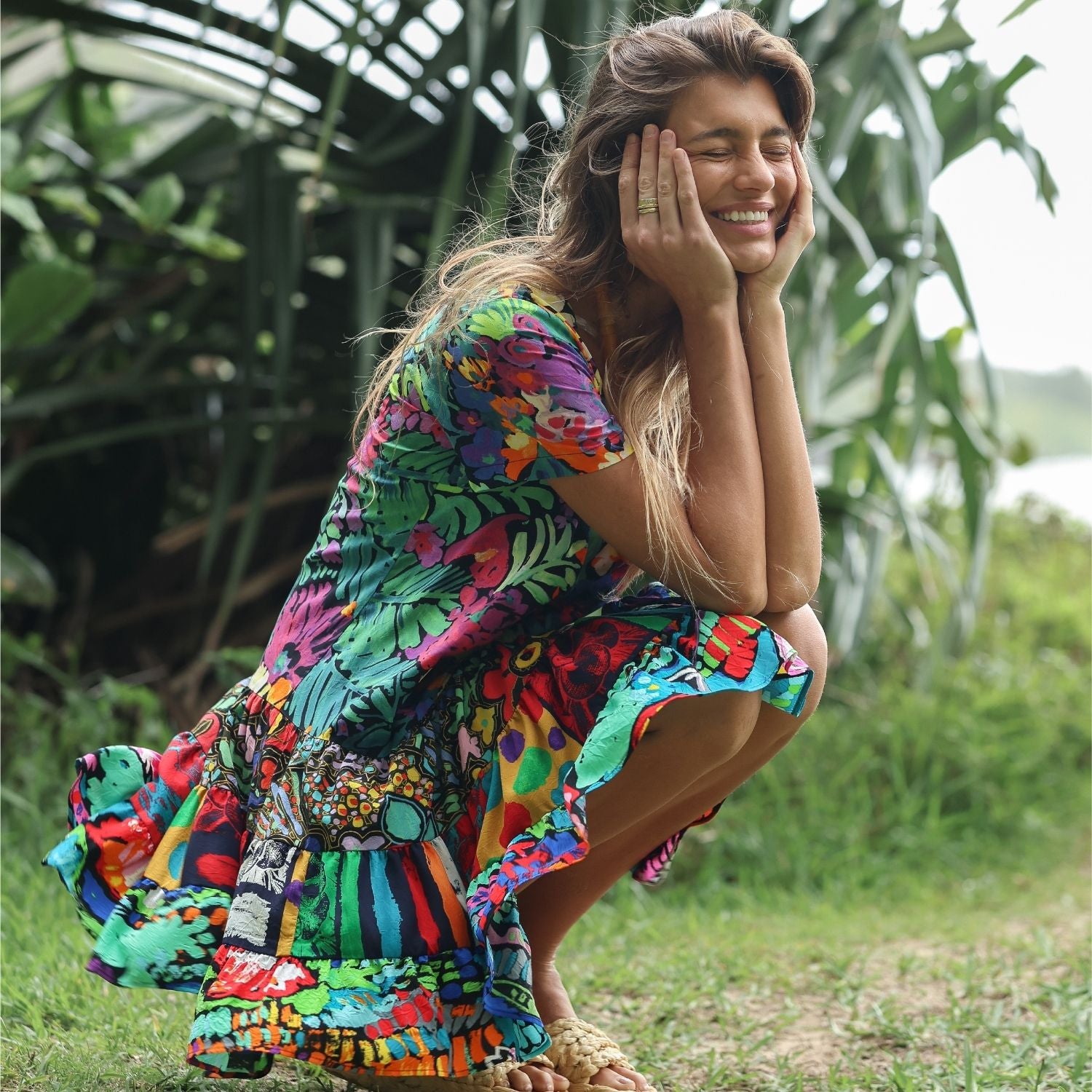 Woman in a colorful dress sitting outdoors with greenery in the background