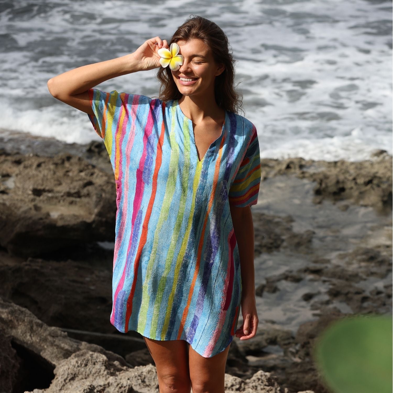 Woman wearing a colorful striped dress standing on a rocky beach.