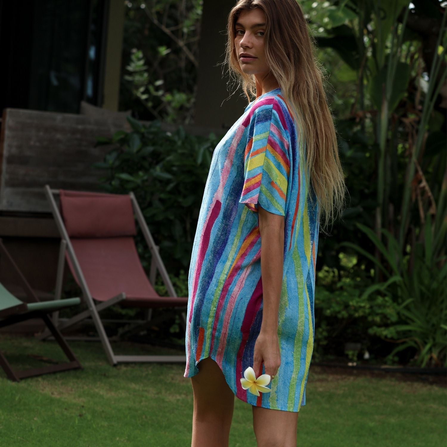 Woman wearing a colorful striped dress with a flower in a garden setting