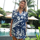 Woman wearing a blue floral dress standing by a pool with palm trees in the background