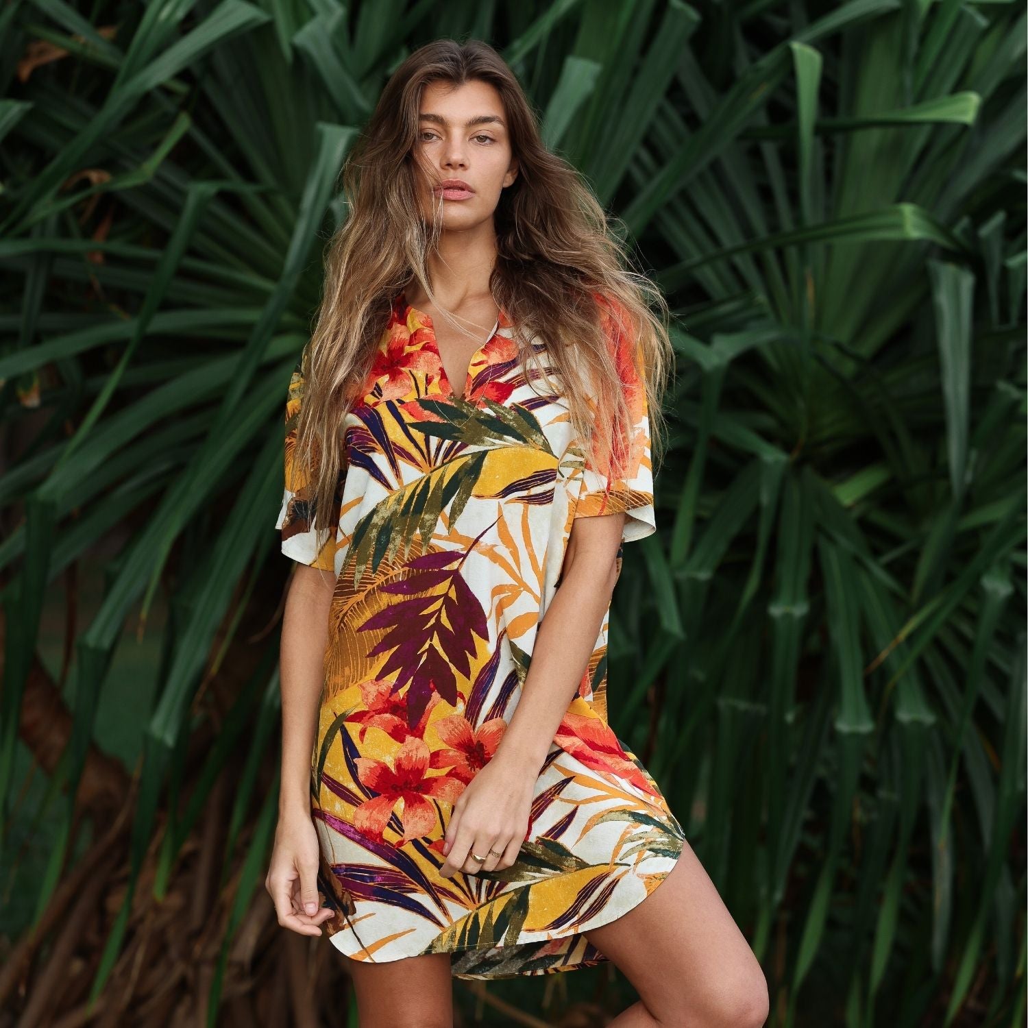 Woman wearing a colorful floral dress standing in front of green foliage