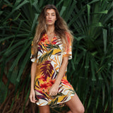 Woman wearing a colorful floral dress standing in front of green foliage