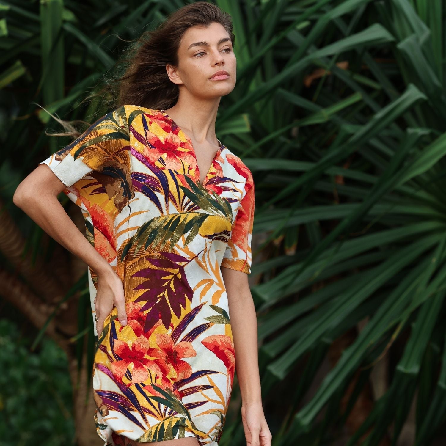 Woman wearing a colorful tropical dress standing in front of green foliage