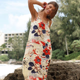 Woman wearing a floral dress standing on a beach with trees and buildings in the background