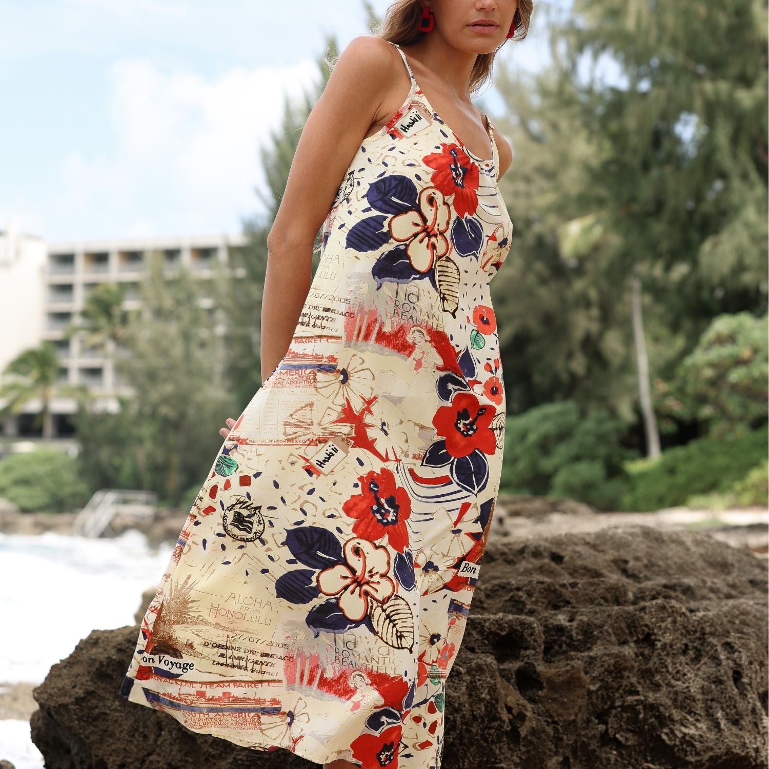 Femme portant une robe à fleurs sur une plage avec des arbres et des bâtiments en arrière-plan