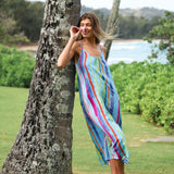 Woman in a colorful striped dress standing next to a tree with a scenic background
