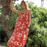 Woman wearing a red floral dress standing among green foliage.
