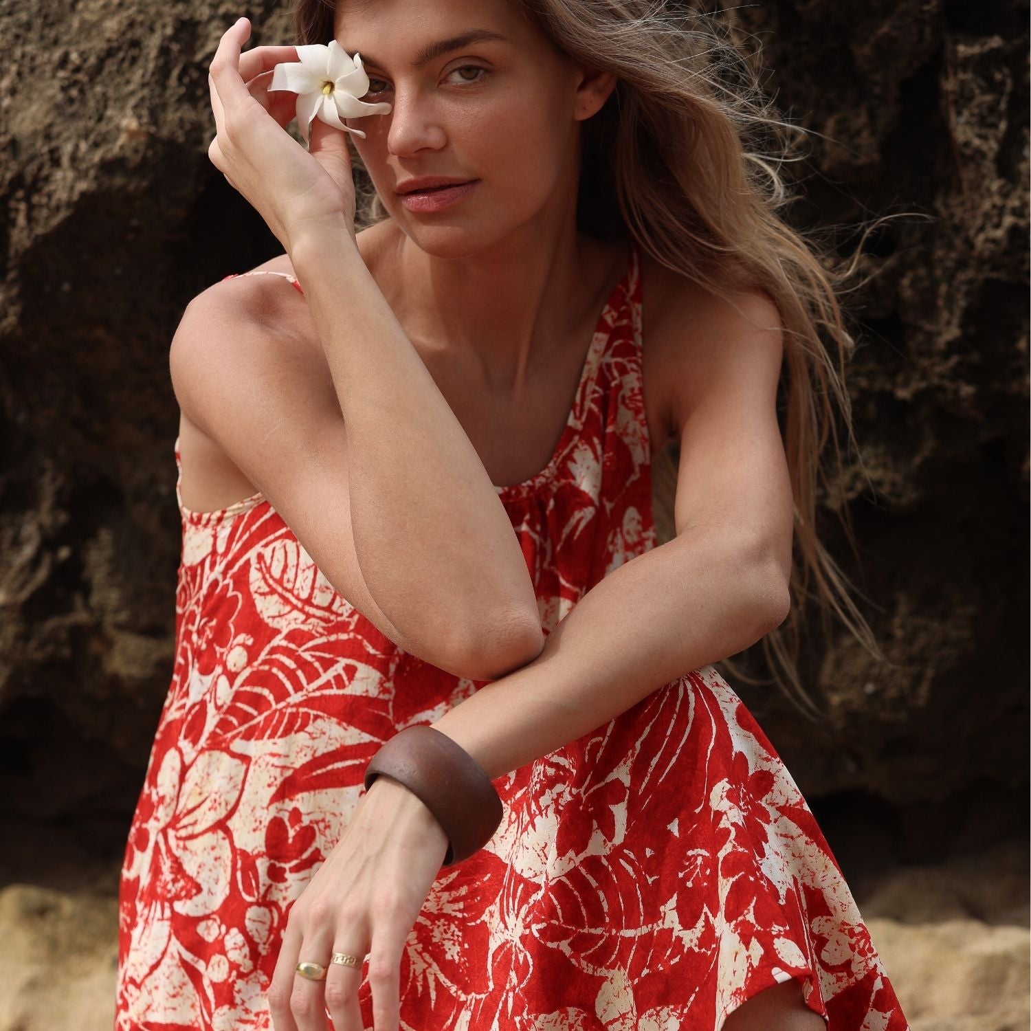 Femme en robe rouge à fleurs tenant une fleur blanche sur fond naturel