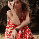 Woman in a red floral dress holding a white flower against a natural background