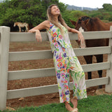 Woman in a colorful floral outfit leaning against a fence with horses in the background