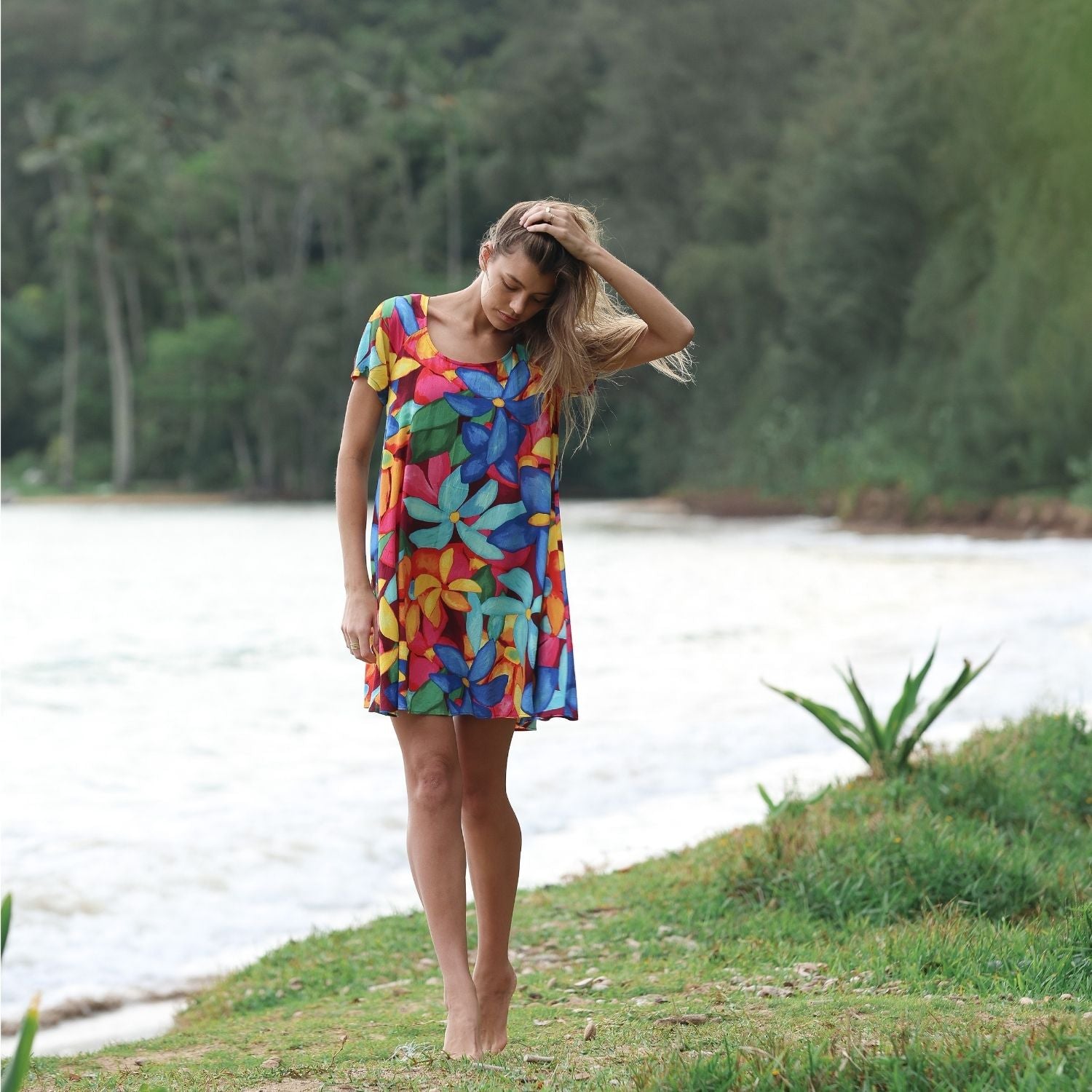 Woman in a colorful dress standing by a body of water with greenery in the background