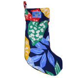 A single christmas stocking featuring a vibrant, abstract tropical leaf pattern in bright colors. The dark blue fabric is covered with large leaves in shades of blue, green, yellow, and white. The stocking has a wide cuff made from the same print, with a small blue "Jams World" logo patch sewn onto it.