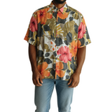 A man wearing a short sleeved, button down Hawaiian style shirt with a large floral print, paired with blue jeans.